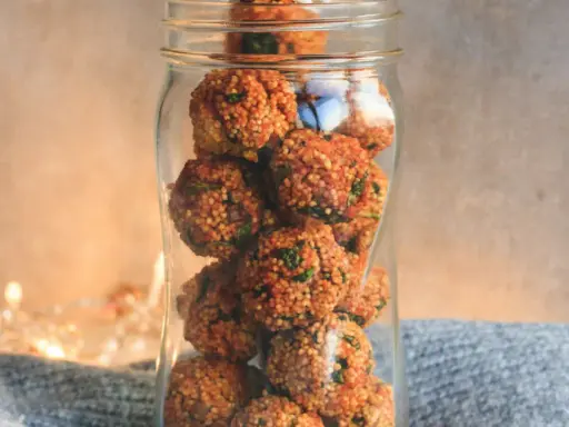 Ein Glas gefüllt mit vielen kleinen, runden Energiebällchen, die mit grünen Kräutern durchsetzt sind.