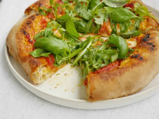 En närbild av en pizza med ruccola och basilika. Perfekt för ett enkelt pizzasås recept.
