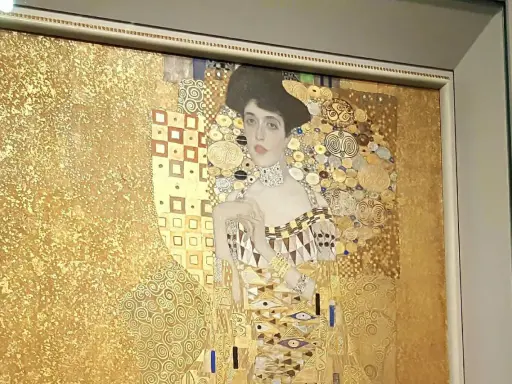 A woman in gold painting, adorned with intricate patterns and jewels, gazes serenely from a gilded background.