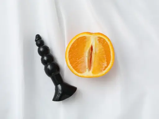Czarny dildo obok przekrojonej pomarańczy, sugerujący orgazm analny.