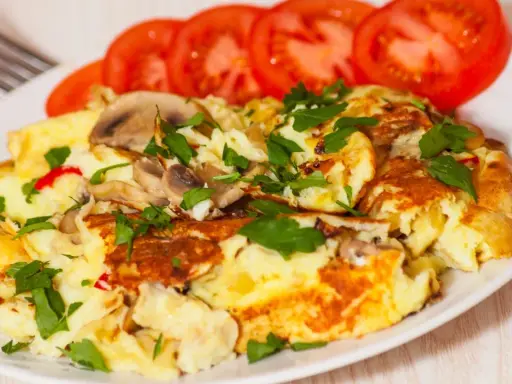 Pyszny omlet jajeczny z pieczarkami i natką pietruszki, podany z plastrami pomidora. Idealny na śniadanie.