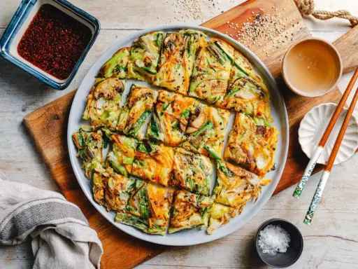 Bunte koreanische Pfannkuchen mit Gemüse, Pilzen und Karotten, serviert mit Dip und Stäbchen.