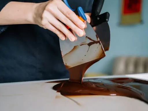Mains travaillant du chocolat brillant sans tempérage avec des spatules. La texture fondante et lustrée promet une gourmandise parfaite.