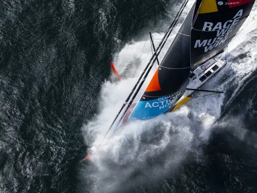 Le voilier de Boris Herrmann fend les vagues, projetant une gerbe d'eau. La voile arbore "Race we must win".