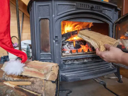 Une main ajoute du bois dans un poêle à bois allumé. Un bon choix de poêle à bois est essentiel pour un hiver chaleureux.