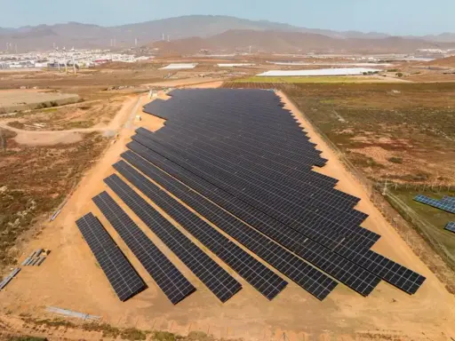 Große Solaranlage in Spanien, die die "Sonnensteuer" umgeht und saubere Energie liefert. Im Hintergrund Windräder und eine Stadt.