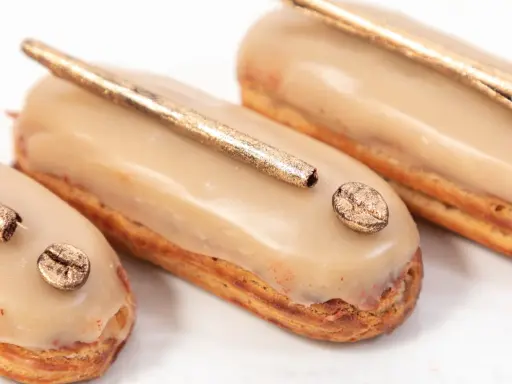Trois éclairs gourmands, glacés à la crème pâtissière café, ornés d'une touche dorée et d'un grain de café scintillant.