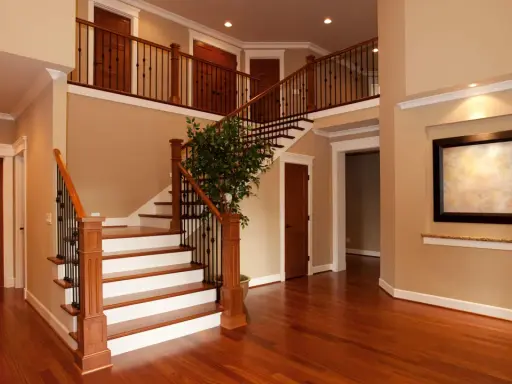 Interno di una casa due piani moderna: scala in legno e metallo, porte in legno, un quadro e un albero decorativo.