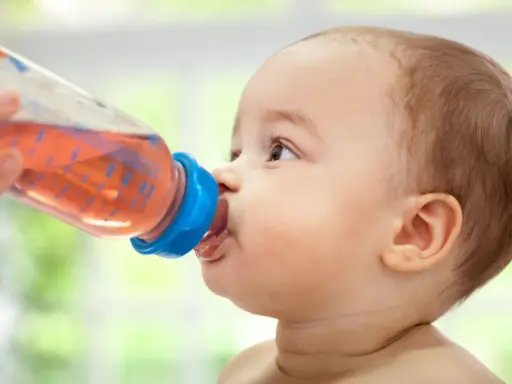 Kleines Baby trinkt aus einer Flasche mit rosafarbenem Tee. Ab wann Tee Baby? Diese Frage stellen sich viele Eltern.