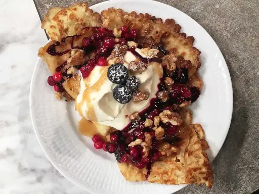 Frasiga pannkakor toppade med vispgrädde, bär, nötter och sirap. En härlig frukost eller dessert.