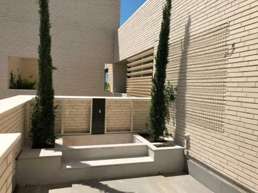 Terraza moderna con cipreses y un retranqueo de fachada que crea un espacio íntimo.