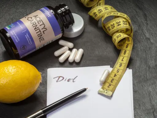 Flasche L-Carnitin, Kapseln, Zitrone, Maßband und Notiz "Diet". Mögliche l-carnitin nebenwirkungen im Blick.