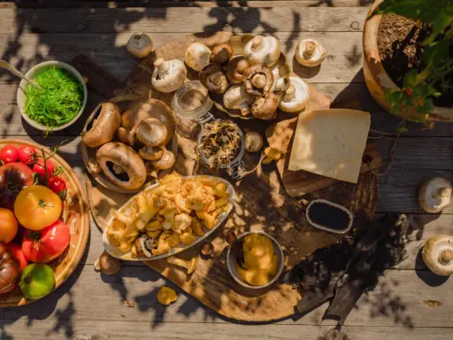 En härlig samling av färska tomater, olika svampar och en bit ost. En skål med gröna alger och en liten skål med mörk sås antyder en djup umami smak.
