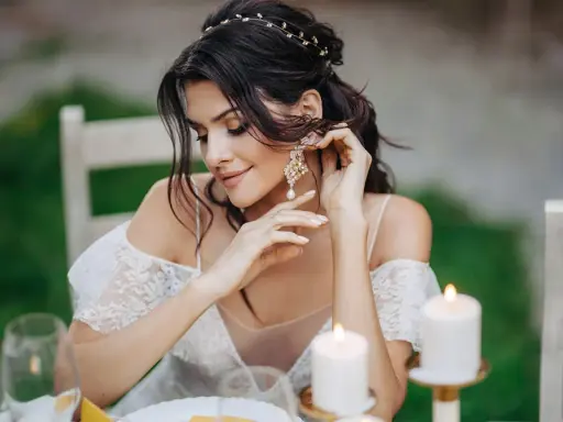 Piękna panna młoda poprawia swoje eleganckie kolczyki ślubne z perłami, przygotowując się do ceremonii.