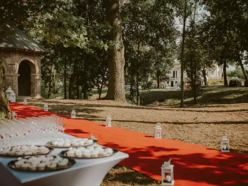 Czerwony dywan prowadzi do pałacu w Małkowie, ozdobiony lampionami i stołem z przekąskami.