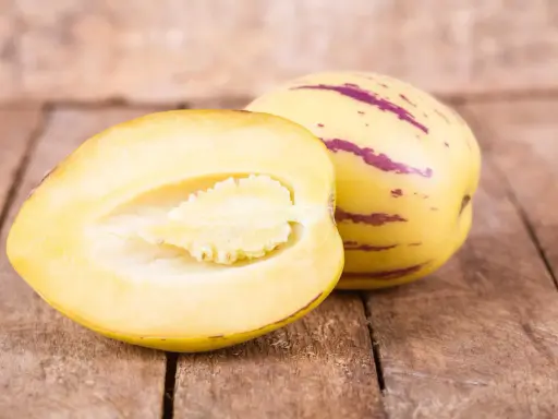 Eine Melonenbirne, die nicht giftig ist, wird auf Holzbrettern präsentiert. Eine Hälfte zeigt das saftige Fruchtfleisch.