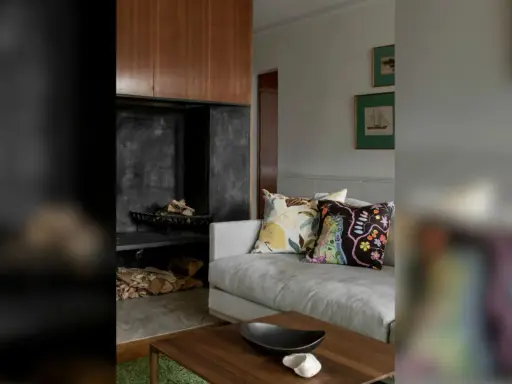En soffa med färggranna kuddar framför en öppen spis med ved. En stilfull inredning som påminner om Josephine Blix design.