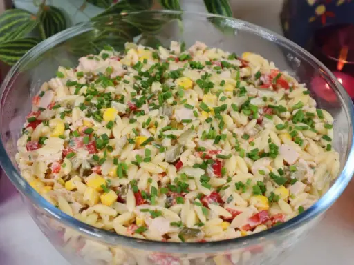 Pyszna sałatka z makaronem orzo, kukurydzą, papryką i kurczakiem, posypana szczypiorkiem. Idealna na letnie dni.