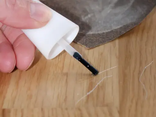Mit einem Lackstift und Schleifpapier werden Kratzer auf dem Laminat repariert.