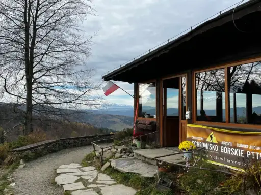 Bacówka pod Wierchomlą, schronisko górskie PTTK z widokiem na góry. Polska flaga powiewa nad wejściem.