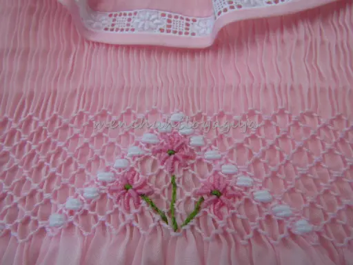 Detalle de puntada smock en tela rosa, con flores bordadas. Aprende como hacer punto smock.