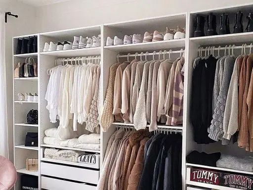 Armarios blancos perfectamente organizados con ropa y zapatos ordenados. Un ejemplo de cómo organizar armarios para un espacio funcional y estético.