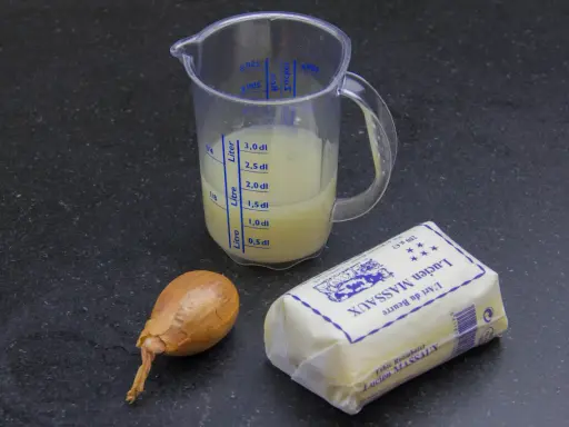 Ingrédients pour un beurre blanc : un oignon, un pichet gradué avec un liquide jaune, et un paquet de beurre Lucien Massaux.
