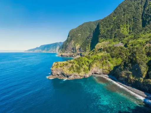 Grüne Berghänge stürzen ins türkisfarbene Meer. Ein perfekter Tag für eine Reise nach Madeira im Oktober.
