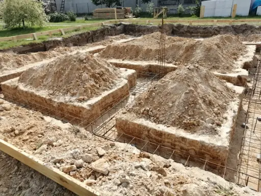 Wykopane fundamenty bez szalunku, z widoczną zbrojeniem i usypaną ziemią.