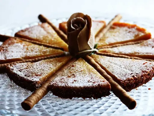 En vacker vit kladdkaka uppskuren i tårtbitar, dekorerad med en pappersros och chokladrullar.