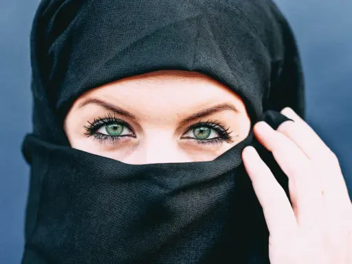 Ein schwarzes Kopftuch umrahmt ein Gesicht, dessen grüne Augen durch den Stoff blicken. Die Bedeutung von Kopftuchfarben ist vielfältig.