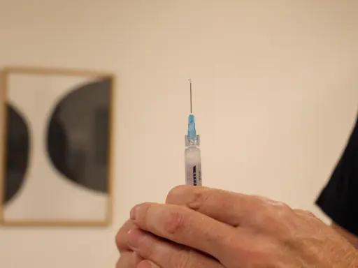 En hand håller en spruta med en droppe vaccin redo för injektion. Kanske en del av vaccin Singapore-programmet.