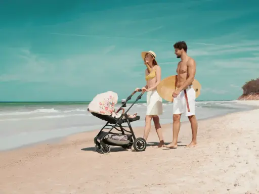 Para spaceruje po plaży z wózkiem Kinderkraft Askoy. Mężczyzna niesie deskę surfingową.
