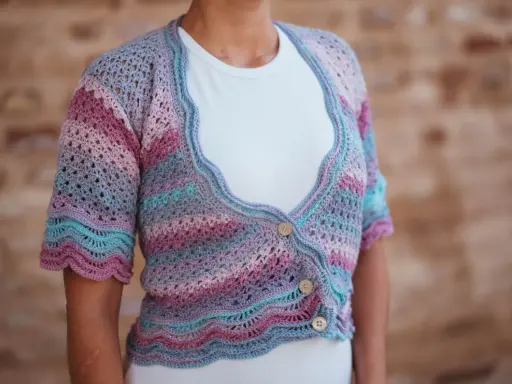 Chaqueta de crochet con rayas degradadas en tonos pastel y delicados puntos calados. Tres botones de madera cierran la prenda.