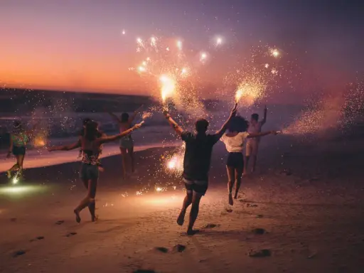 Giovani festeggiano il Ferragosto sulla Riviera Romagnola con scintille sulla spiaggia al tramonto.