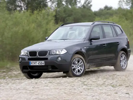 Ciemnoszary BMW X3 2024 na szutrowej drodze, otoczony zielenią.