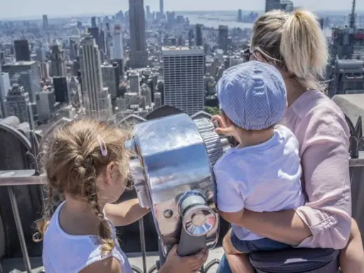 Familia disfrutando de las vistas de Nueva York con niños, explorando la ciudad a través de un telescopio.