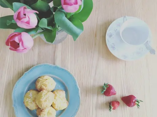 Chouquettes traditionnelles sur une assiette bleue, accompagnées de fraises et d'un bouquet de tulipes roses. Parfait pour une pause gourmande.