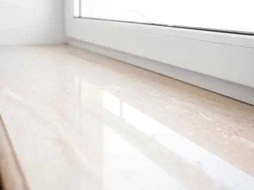 Jasny parapet z polerowanego konglomeratu granitowego, odbijający światło.