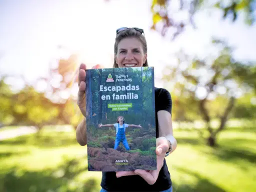 Mujer sonriente muestra libro "Escapadas en familia", con un niño en portada, ideal para viajes inolvidables para niños por España.