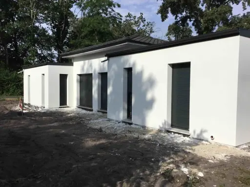 Maison moderne avec toit plat, plan de 150m2. Construction blanche aux lignes épurées, entourée d'arbres.
