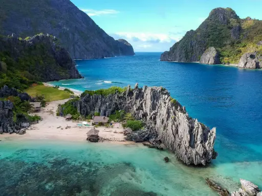 A secluded beach in the Philippines, with turquoise waters, limestone cliffs, and small huts. A perfect gay getaway in paradise.