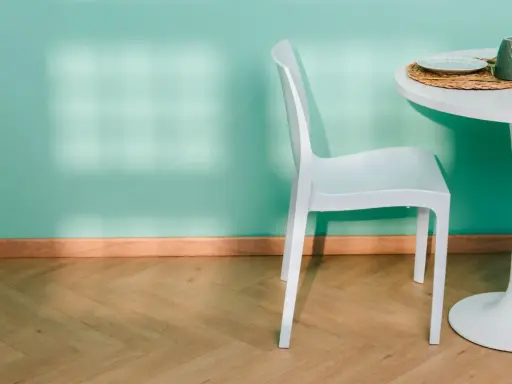 Un battiscopa in legno chiaro completa l'arredamento di una stanza con parete verde acqua, sedia bianca e tavolo.