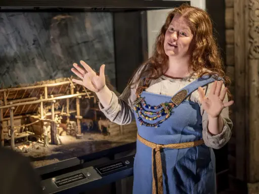 En guide i vikingakläder berättar vid en modell av en vikingaby på ett wikinger museum i Stockholm.