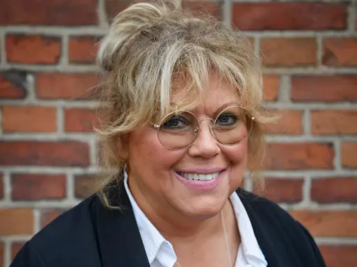 Marie Nilsson Lind ler mot kameran, med sitt blonda hår uppsatt och runda glasögon.