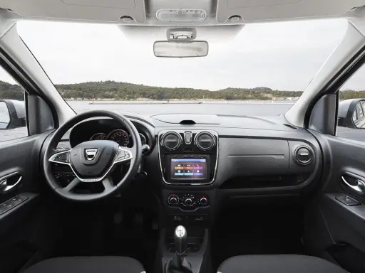 Interior del Dacia Lodgy con volante, pantalla táctil y palanca de cambios. El paisaje marino se ve a través del parabrisas.