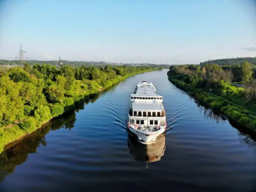 Nave da crociera solca un fiume sereno, con rive alberate che ricordano la bellezza naturale vicina alla capitale Russia.