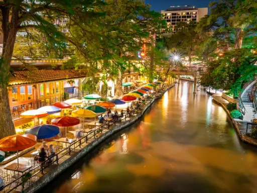Bunte Sonnenschirme säumen den River Walk in San Antonio, wo Gäste abends in Restaurants am Wasser speisen.