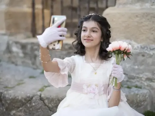 Dziewczynka w sukni komunijnej robi selfie z bukietem kwiatów. To ważny moment, przygotowania do pierwszej komunii świętej krok po kroku.