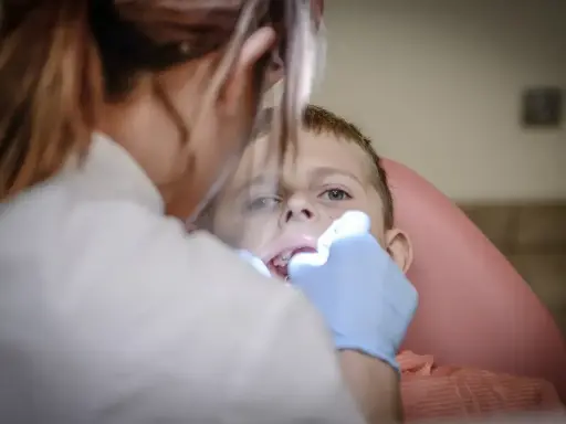 Chłopiec nie chce otworzyć ust u dentysty. Stomatolog próbuje go zbadać.